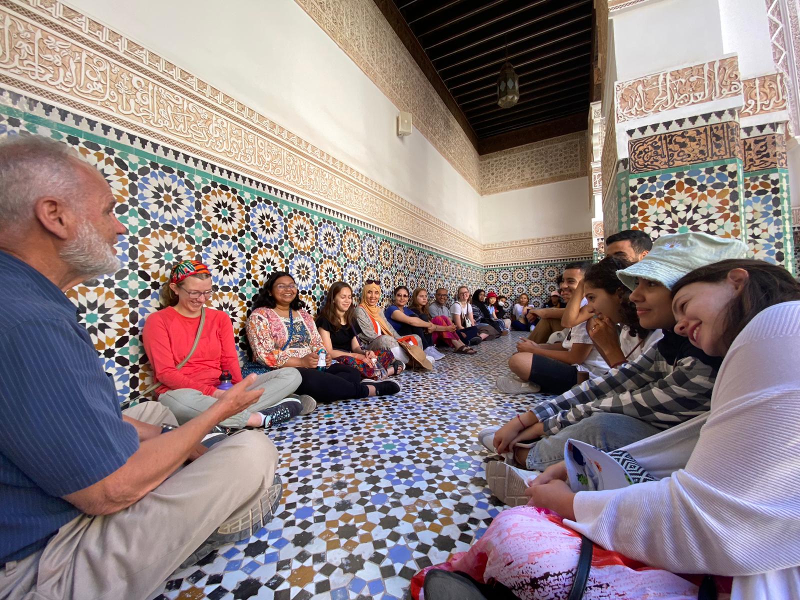 A group of students sit in a circle in a room full of beautiful tile work.