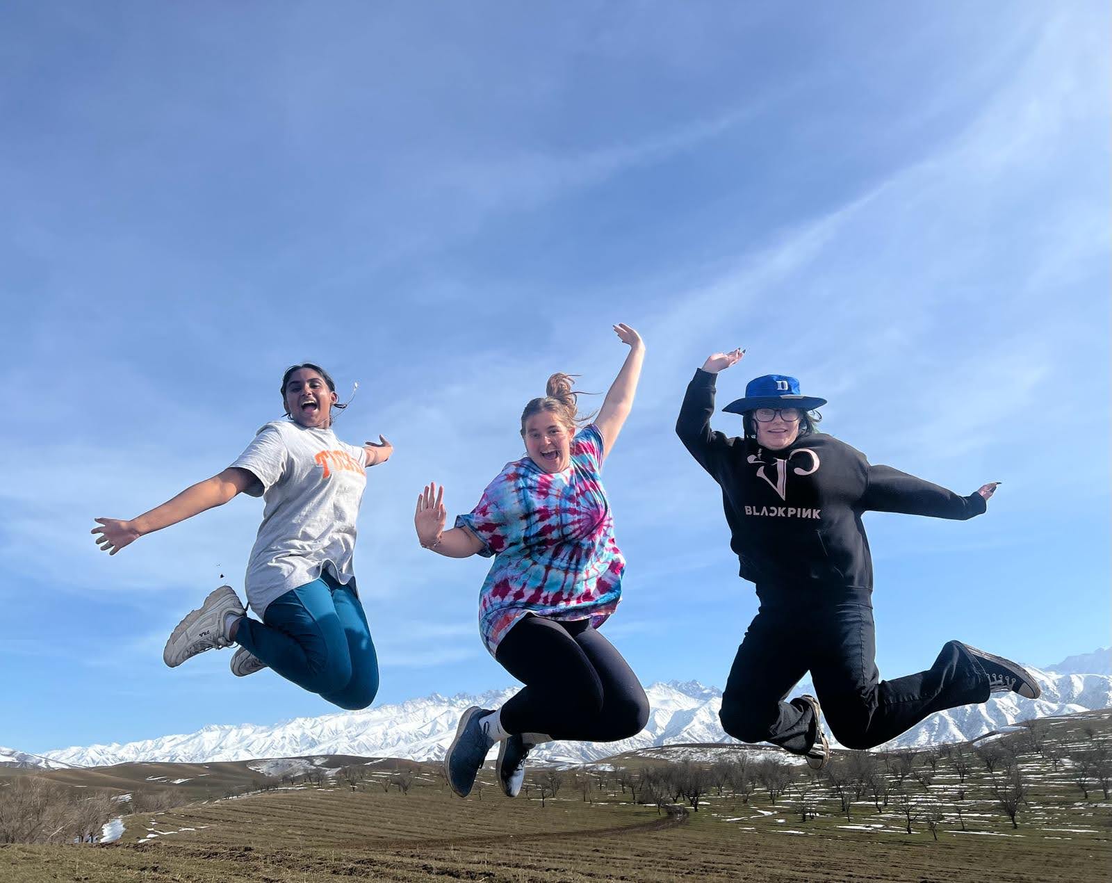 Three NSLI-Y participants jumping in the air, smiling in front of a blue sky and snowy mountains.