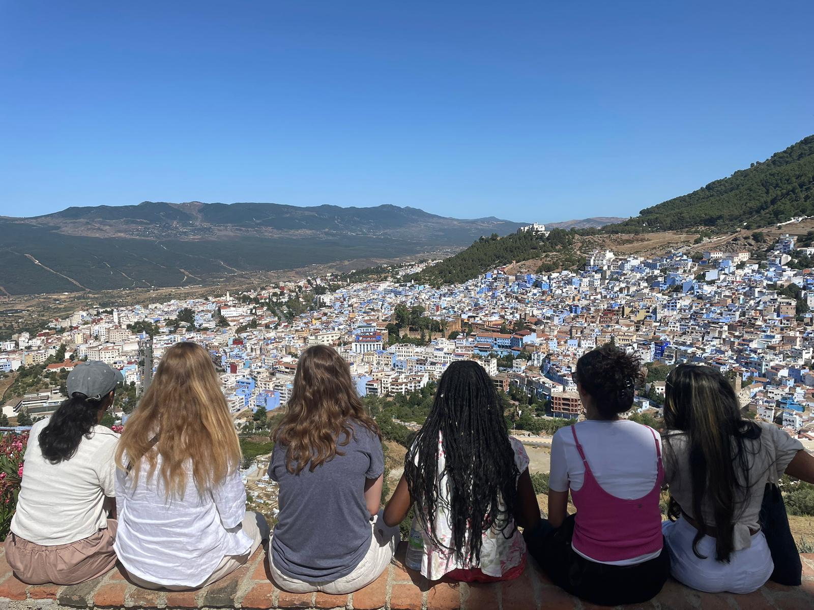 An image of six students overlooking a dense city nestled in a lush valley