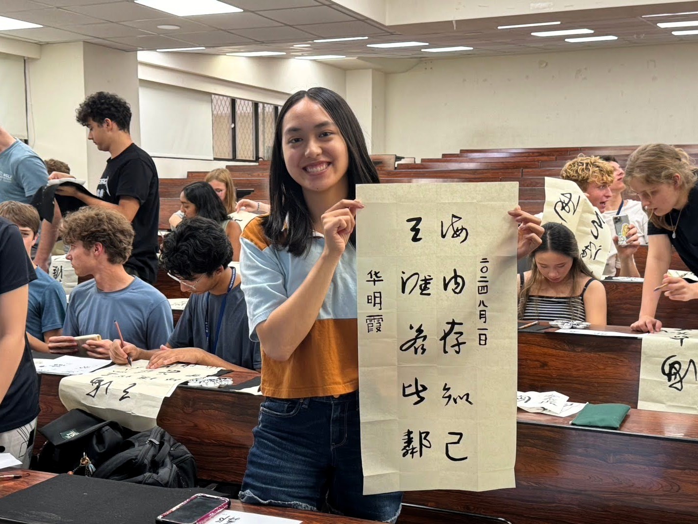 An image of a student showing off her Chinese calligraphy as students practice around her