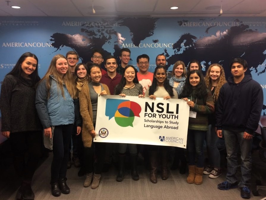 NSLI-Y alumni representatives stand in a group in front of an American Councils background and hold a NSLI-Y banner