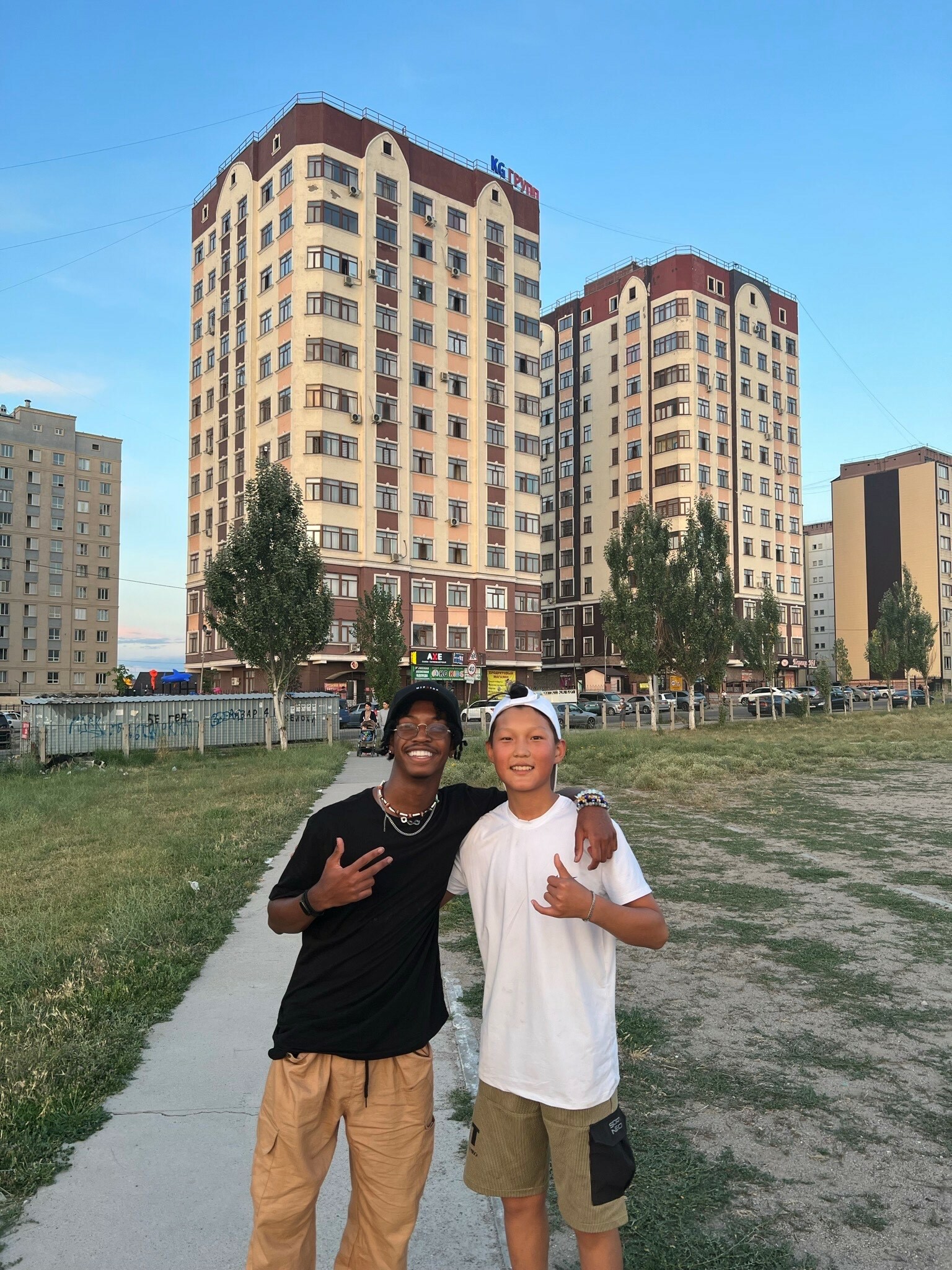 Two students smile for the camera in front of tall apartment buildings
