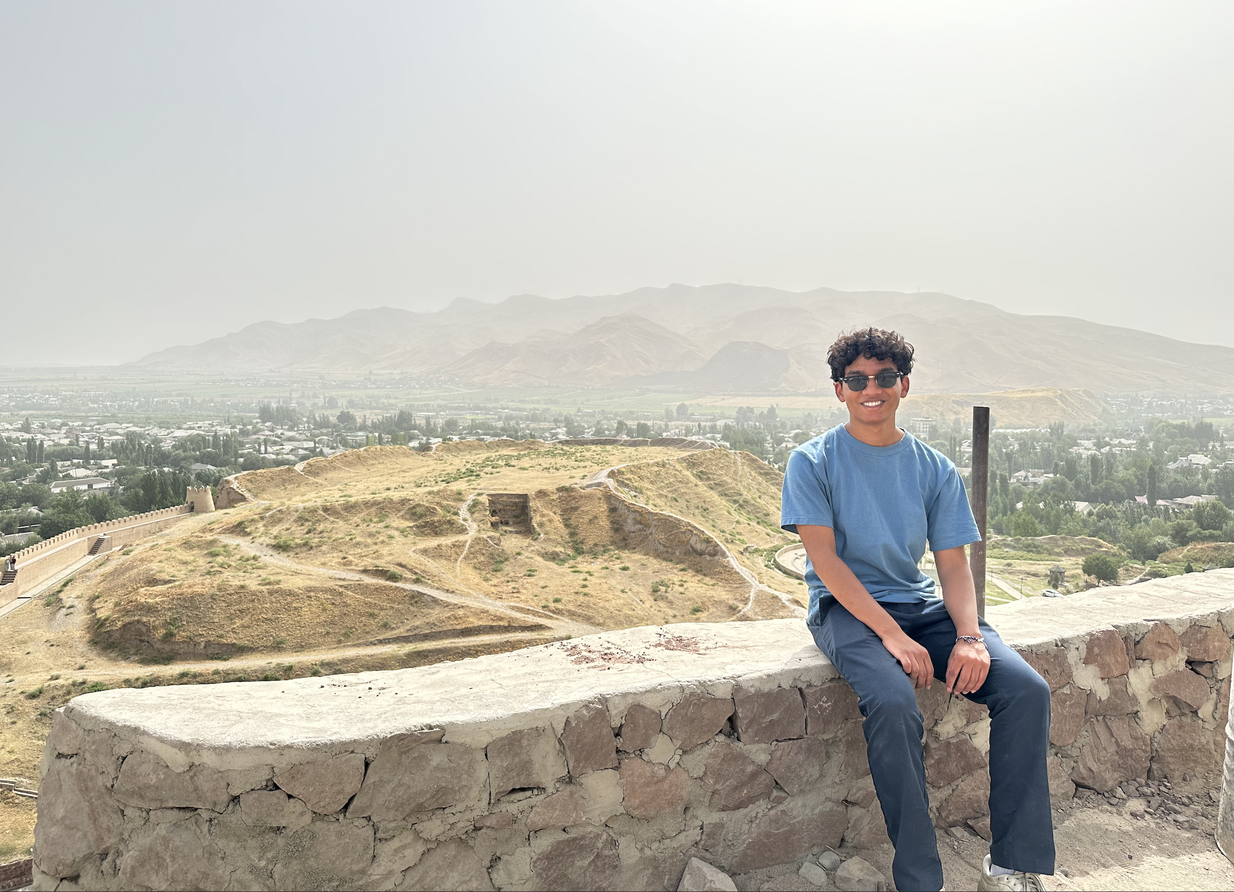 A NSLI-Y alum sits on a rock wall overlooking a valley