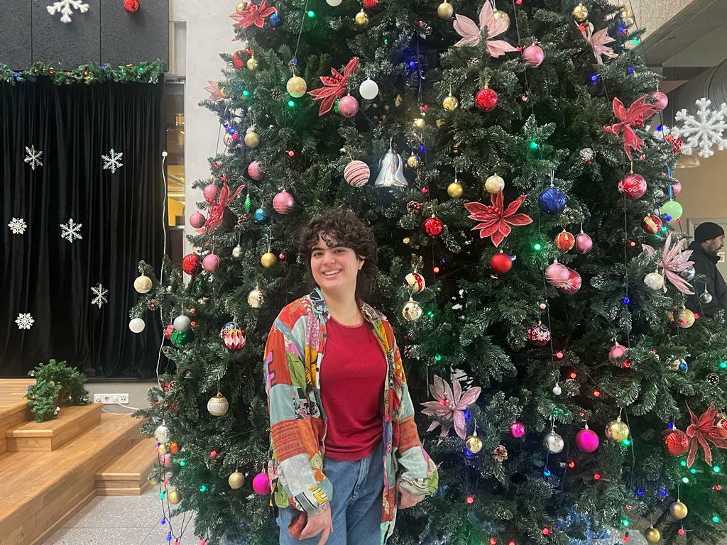 A student stands in front of a decorated Christmas tree