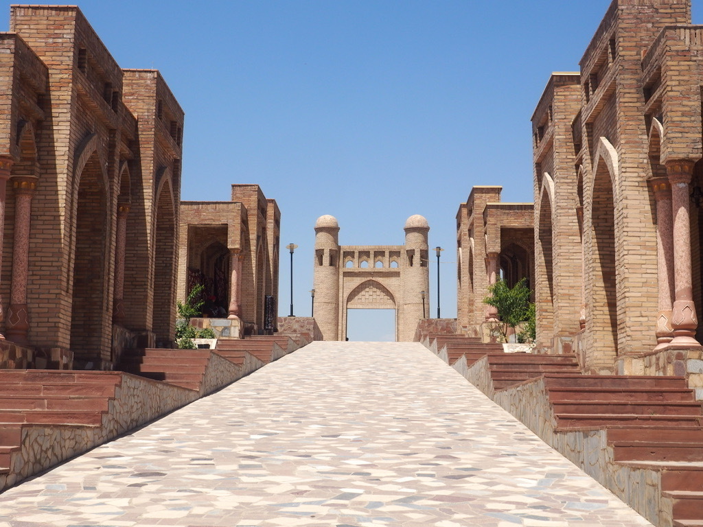 a symmetrical image along a walkway among columns outside leading to a gate