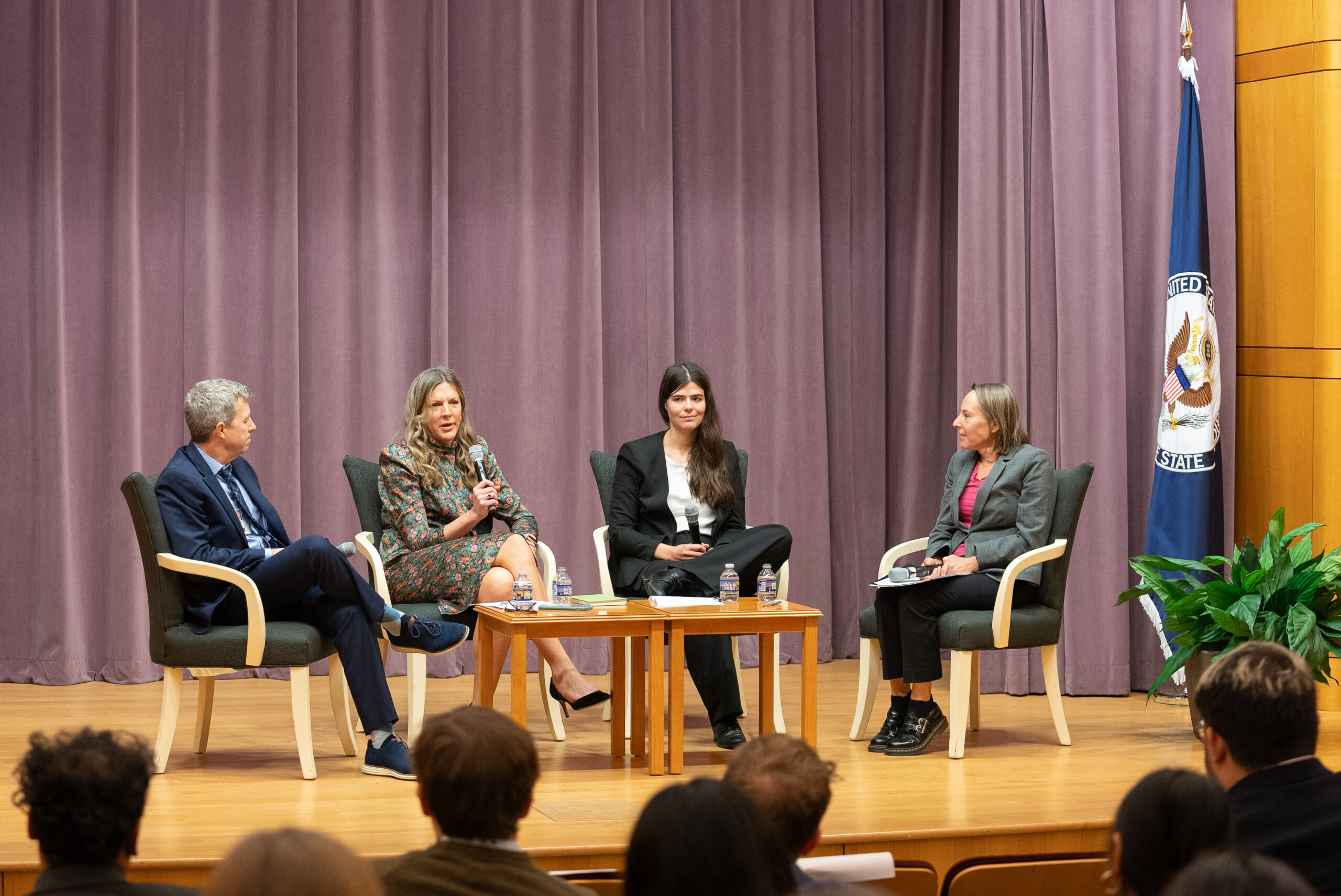 Four seated panelists speak onstage before an audience