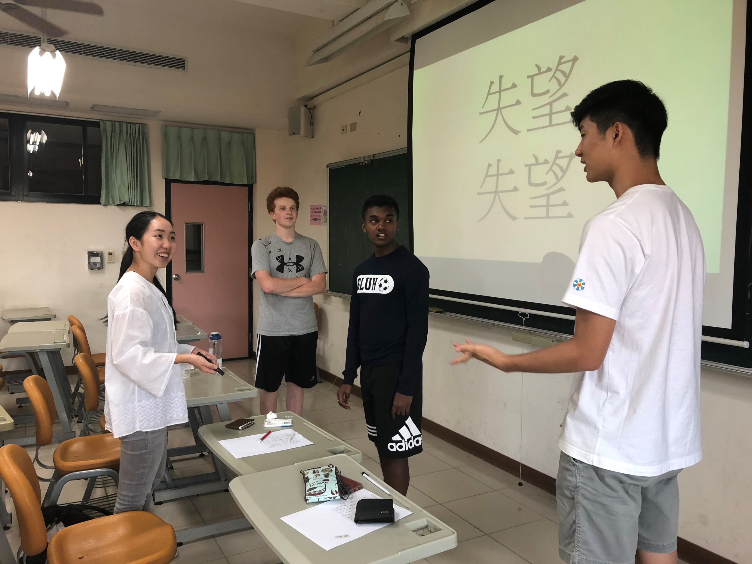 Three NSLI-Y students standing engaging with NSLI-Y teacher in front of Chinese characters.