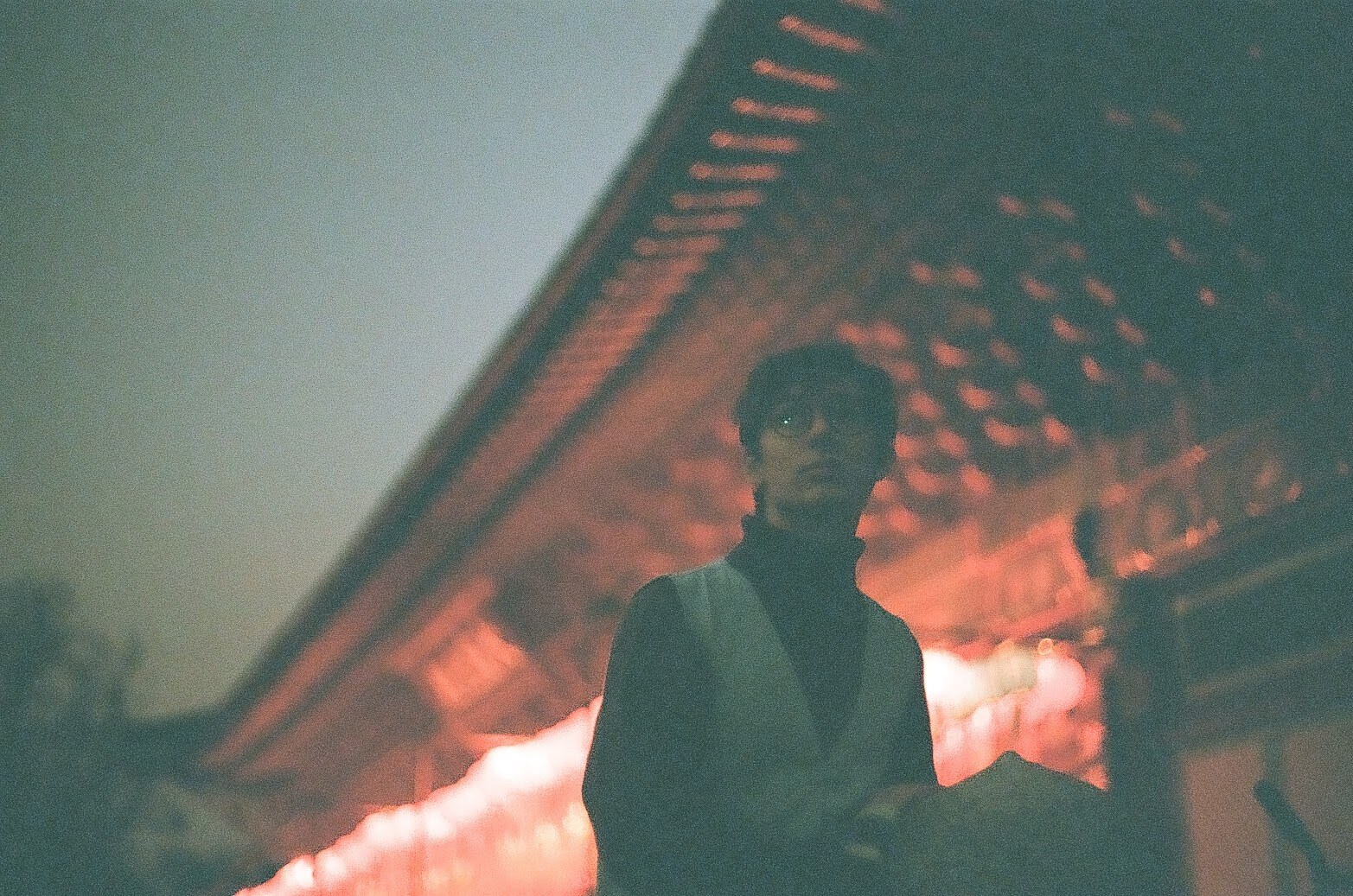 Ellie stands in front of a Buddhist temple in Korea. He stands in front of a building with red light and intricate architecture.