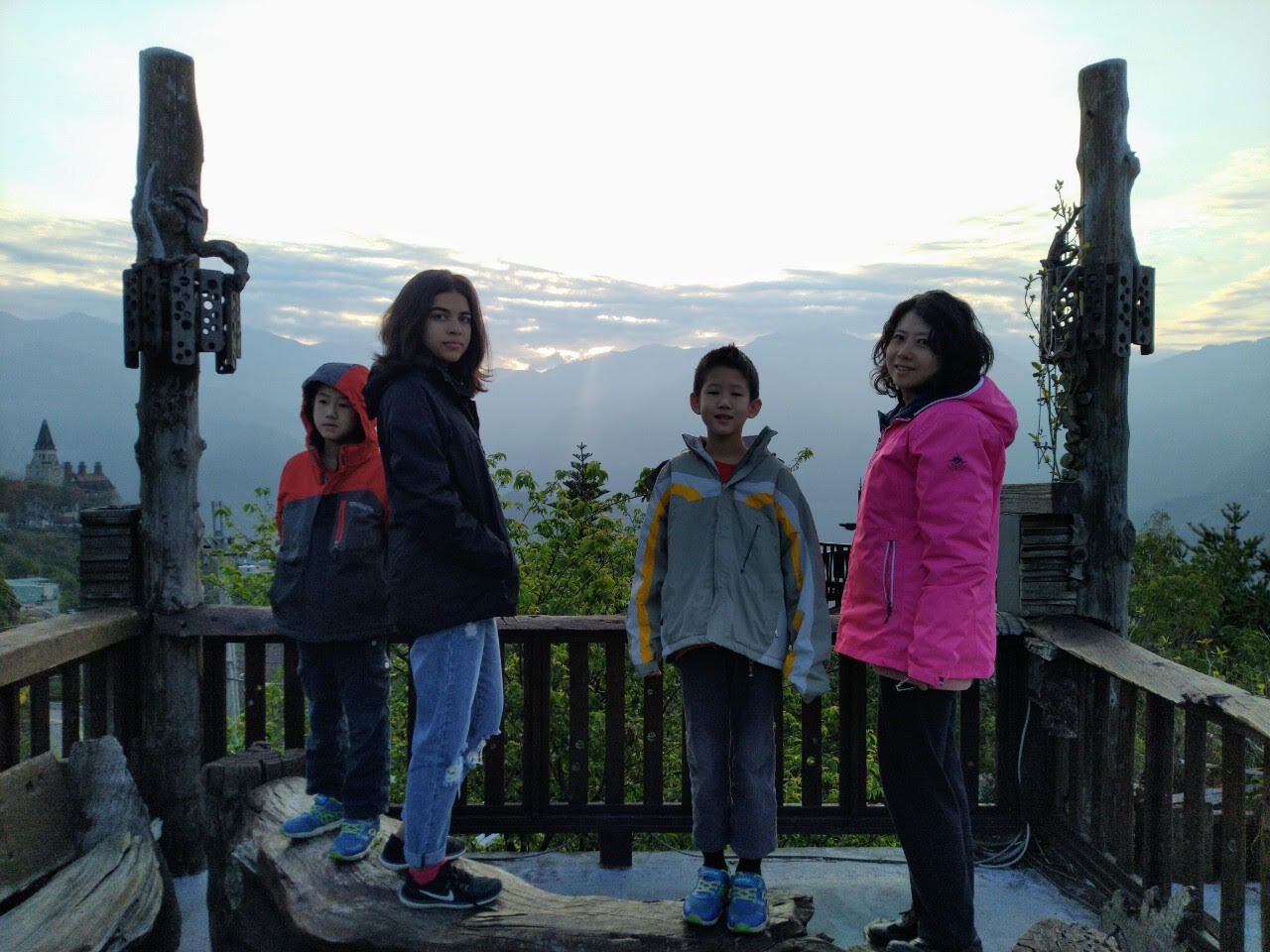 An image of Hannah with peers standing at the top of a mountain with trees in the background and the sun behind