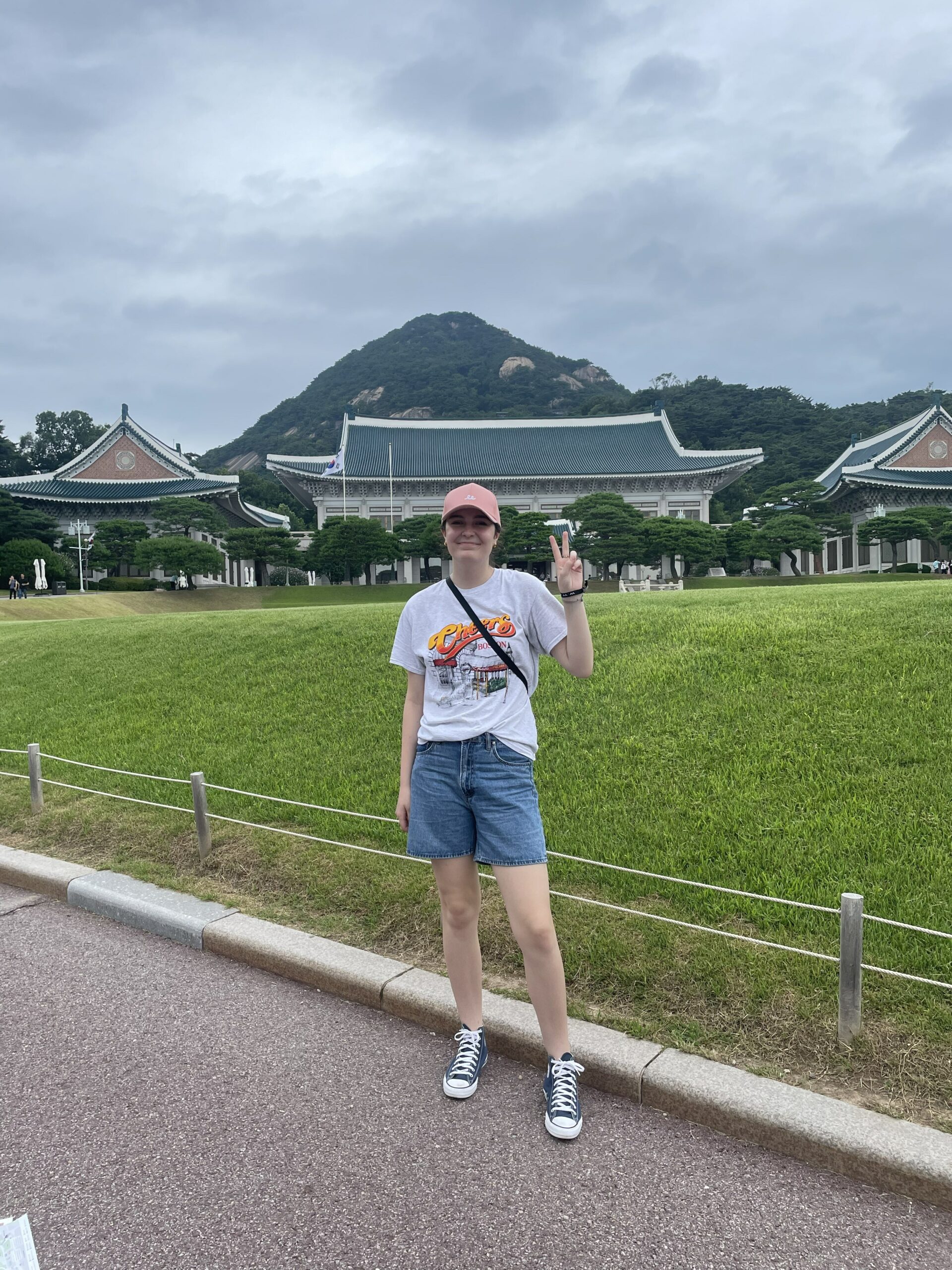 A student poses before a grassy fields with houses and a mountain in the background