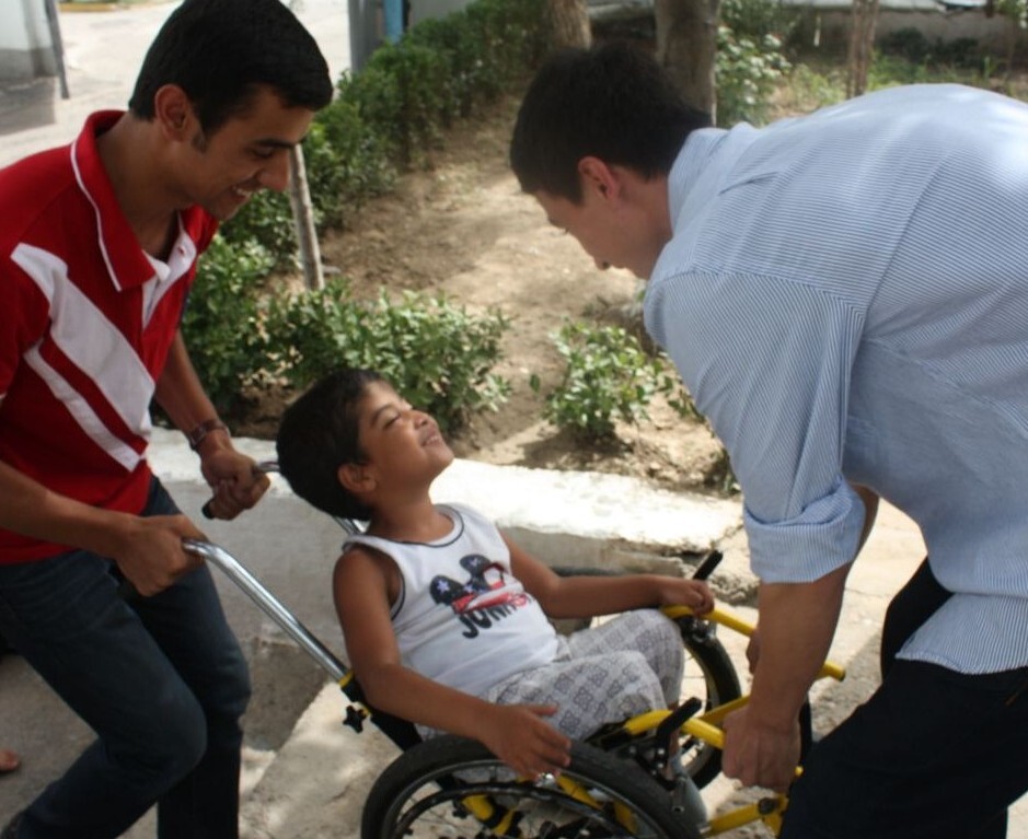 image of two nsli-y students helping a child in a wheelchair