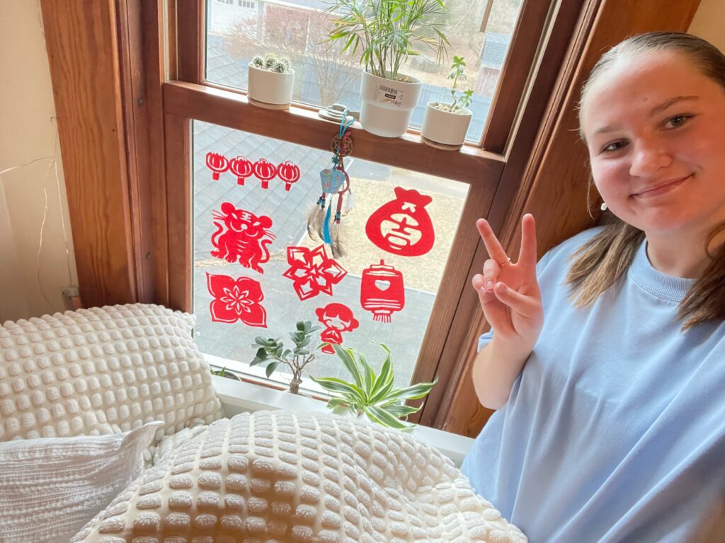 VNSLI-Y Student poses with red paper that has been cut in intricate designs in traditional Chinese designs.  