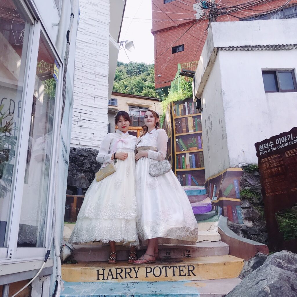 Annalise stands with another young woman on the streets of Busan, South Korea. Both are wearing traditional white dresses.