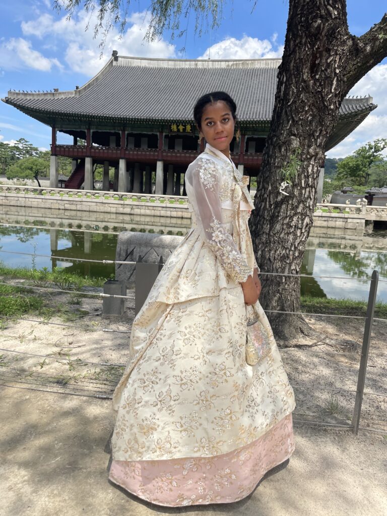 A young woman is dressed in a traditional Korean outfit and stands in front of a temple in South Korea.