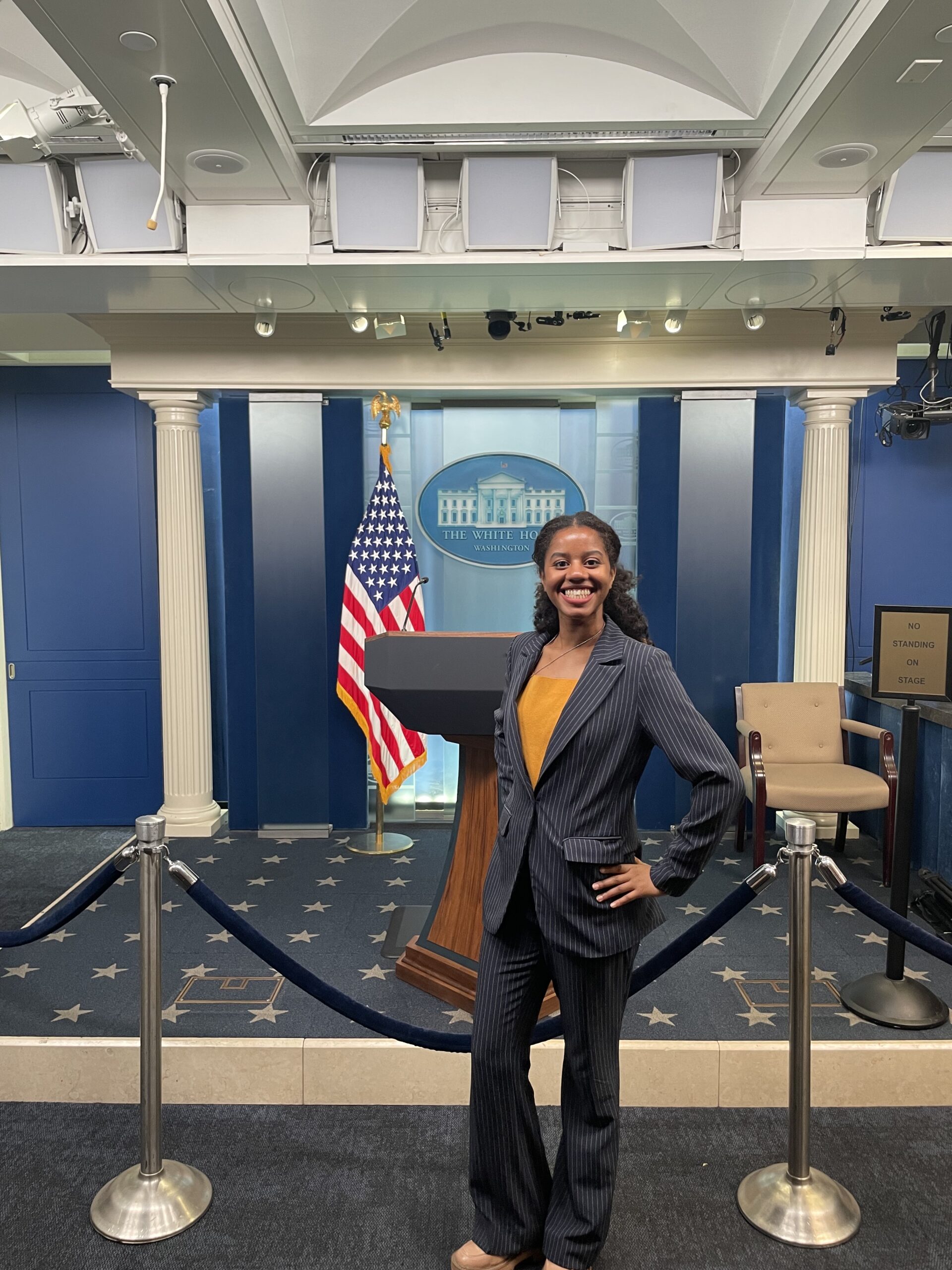 A young woman in a suit stands in front of a podium at the White House